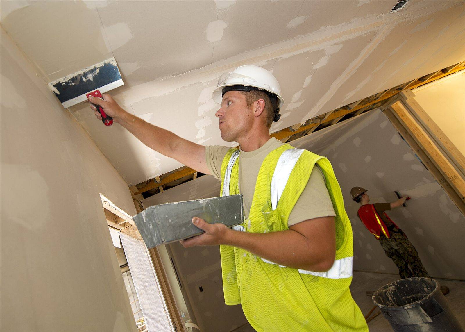 A worker spreading joint compound on a new drywall ceiling