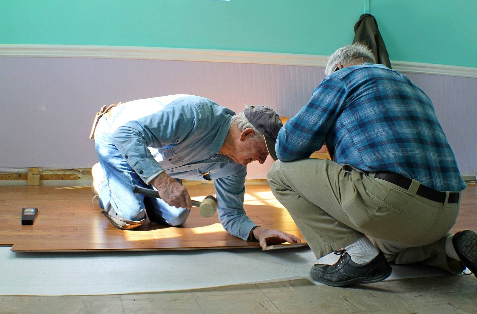 Two men on their knees fitting laminate floor planks over underlayment