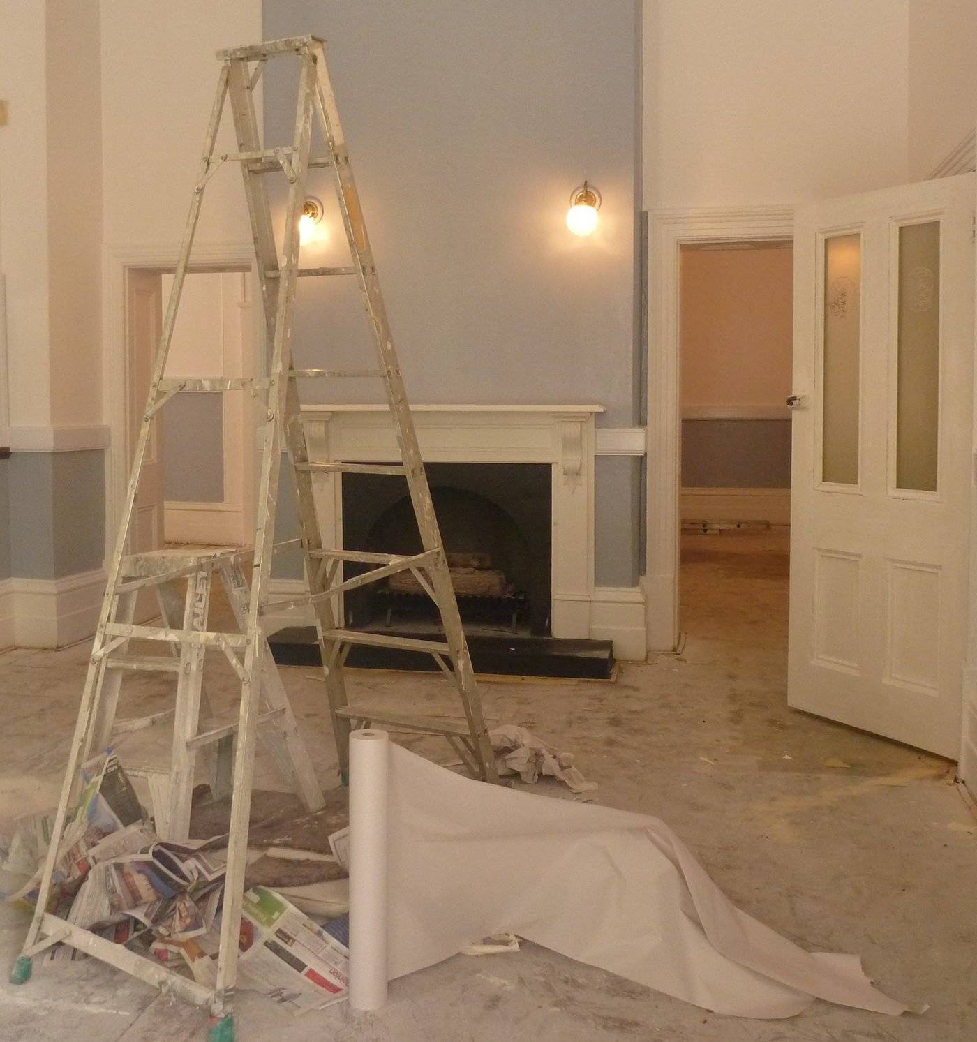 A room part way through painting, with a stepladder and floor paper in front of a fireplace