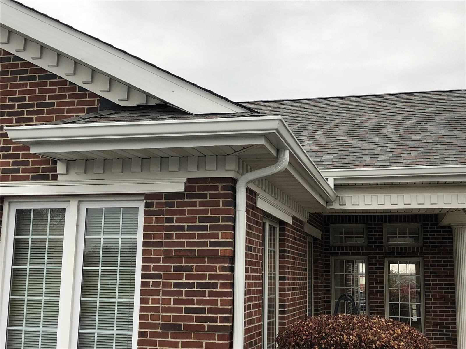 New white gutter and downspout fixed along the eaves of a brick house