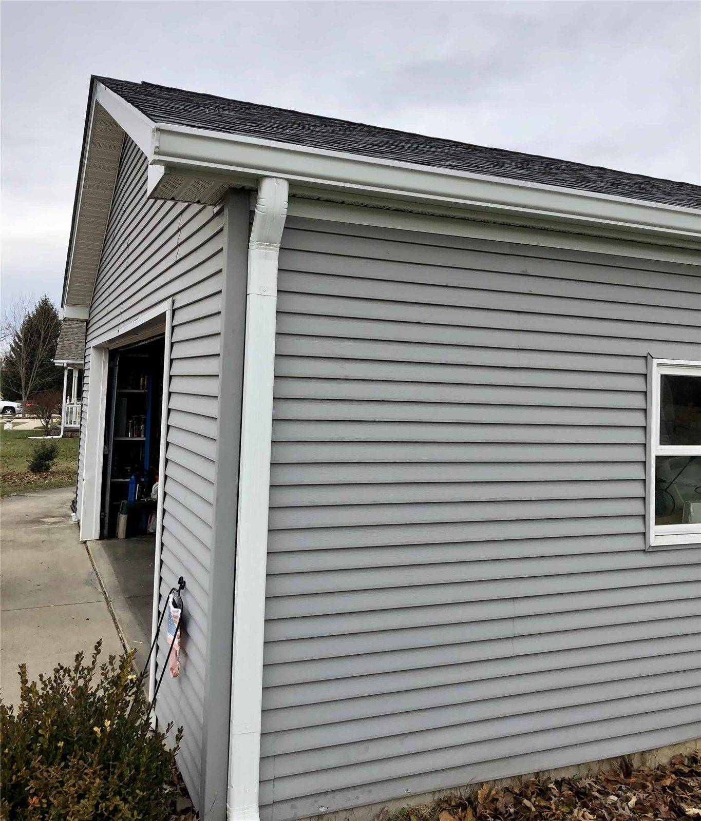 Corner of a garage in new gray vinyl siding with a white gutter above