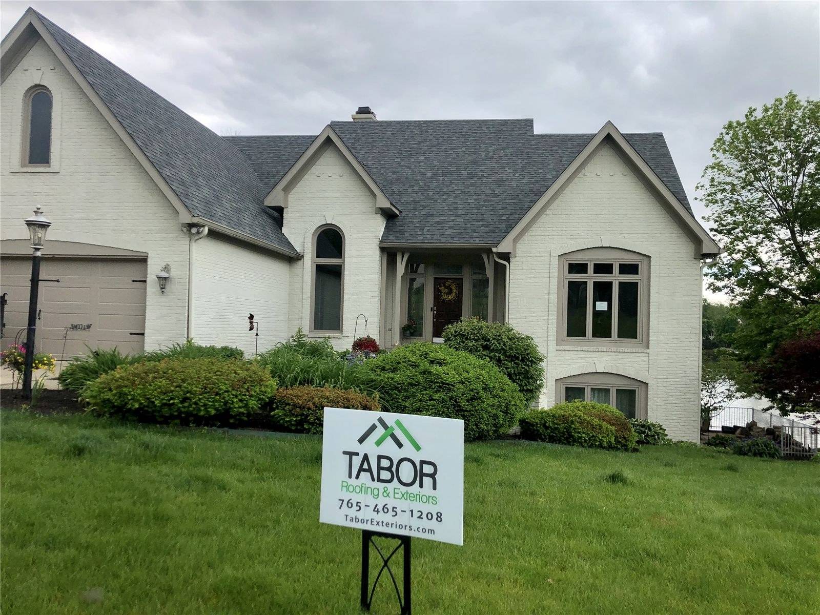 White painted brick house with a new charcoal shingle roof and a Tabor yard sign on the lawn